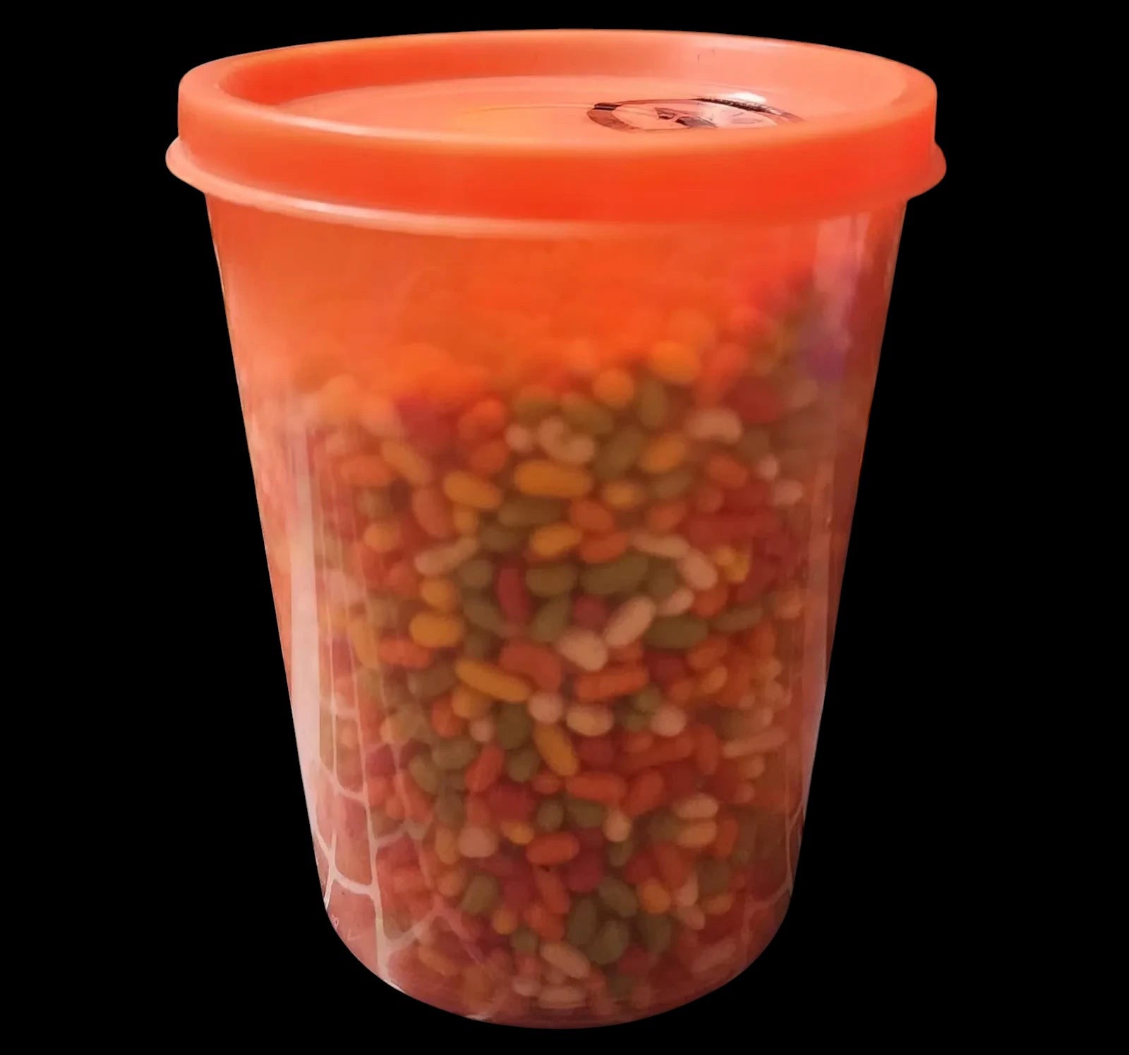 Desipan assorted candy-coated seeds in a bright orange plastic container. Mix of red, orange, yellow, and green seeds.