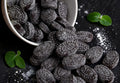 Desipan black licorice candies dusted with sugar, oval-shaped with embossed pattern.