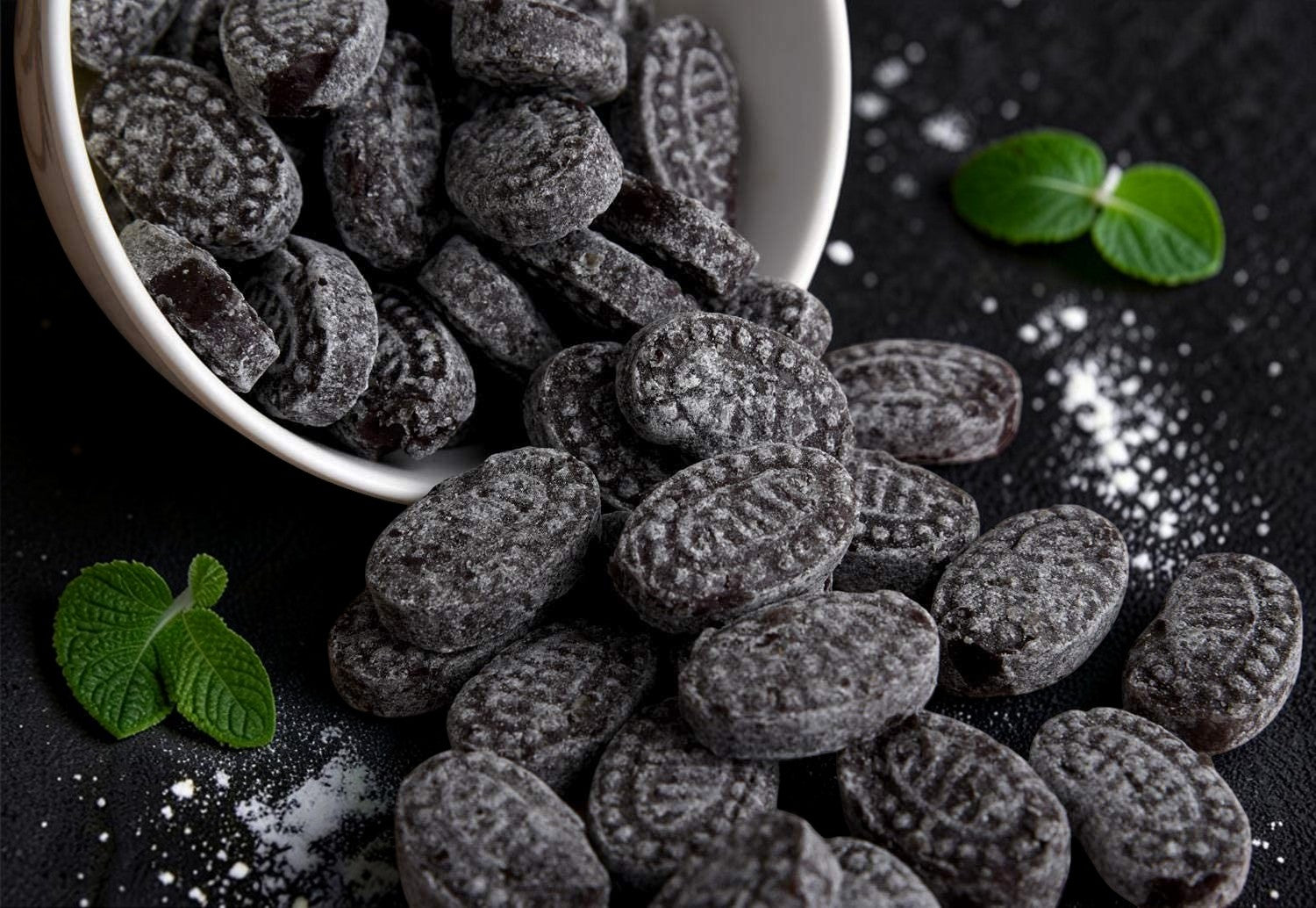 Desipan black licorice candies dusted with sugar, oval-shaped with embossed pattern.