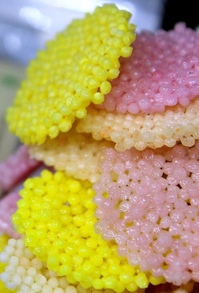 Desipan artisanal crispy sago papadum crackers in vibrant yellow and soft pink colors with a light, airy texture.