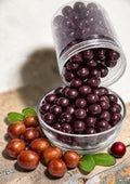 Desipan dark chocolate covered jujube fruits in a glass bowl with fresh jujubes and mint leaves.