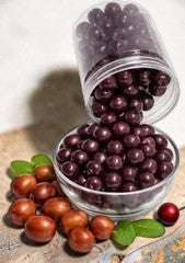 Desipan dark chocolate covered jujube fruits in a glass bowl with fresh jujubes and mint leaves.