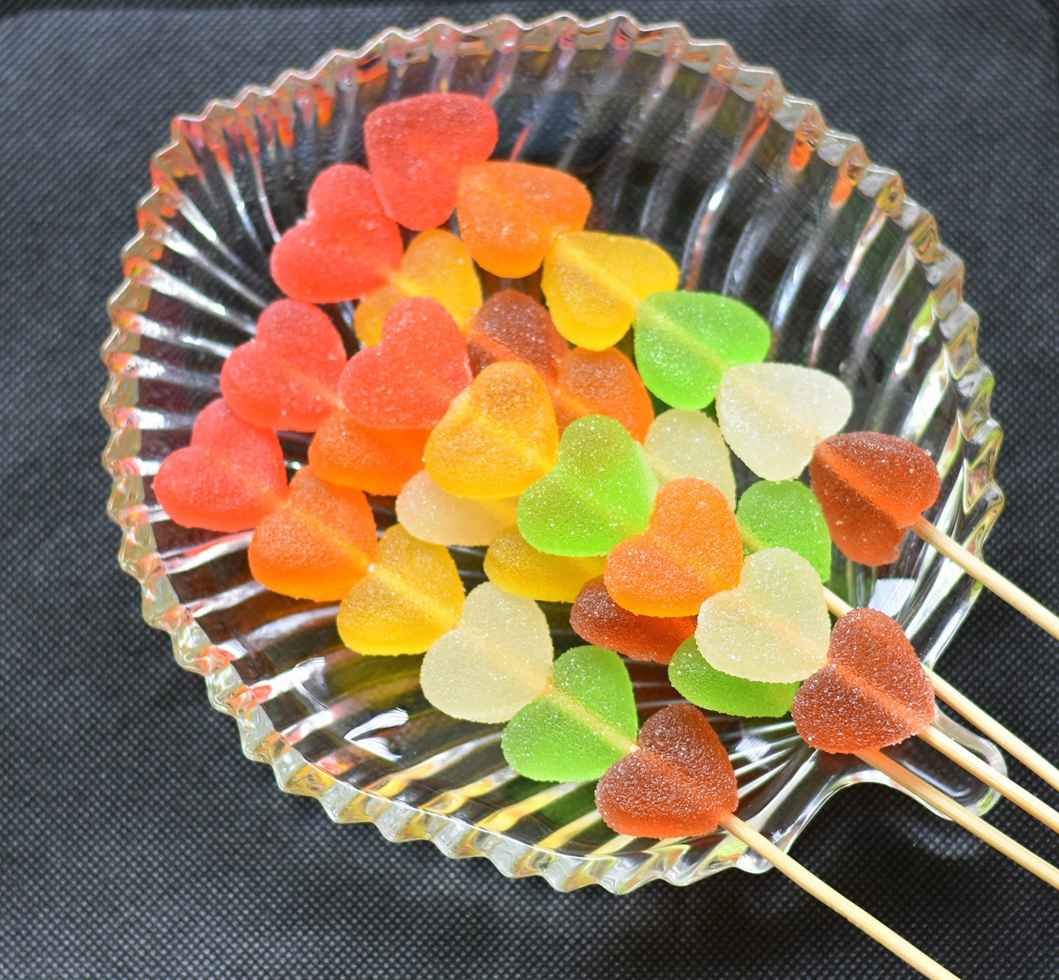 Desipan assorted fruit flavored gummy heart lollipops coated in sugar, served in a glass dish.