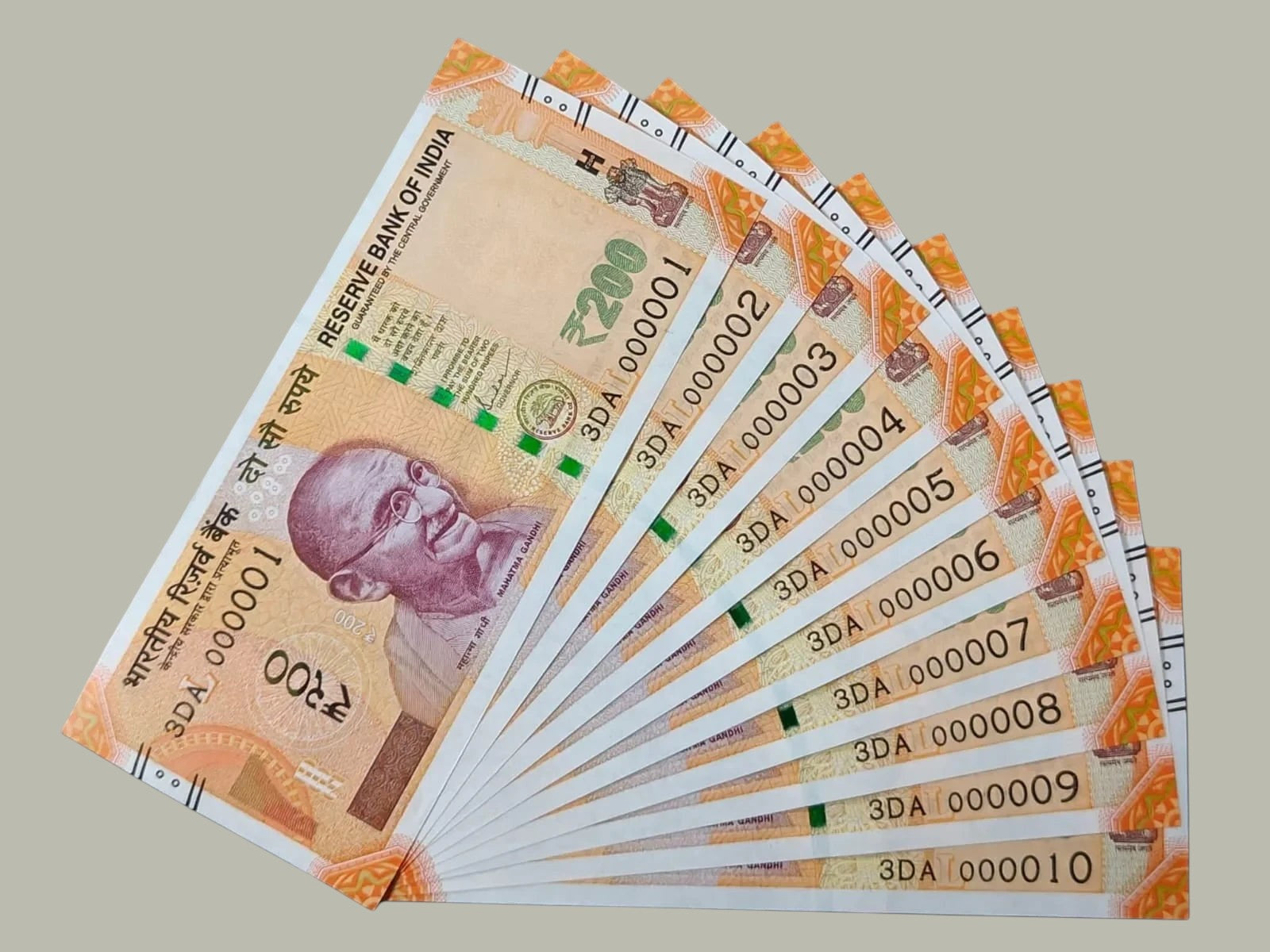 Desipan Indian 200 Rupee banknotes collection featuring Mahatma Gandhi portrait, orange and yellow hues, and serial numbers 000001-000010.