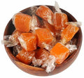 Desipan orange flavored hard candy pieces individually wrapped in clear cellophane, served in a wooden bowl.