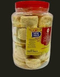 Desipan Soan Papdi Indian sweet pastry snacks in a clear plastic jar with a red lid. Flaky, square-shaped sweets.