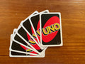 Desipan UNO card game with red and black cards fanned out on a wooden surface. Features the iconic UNO logo.