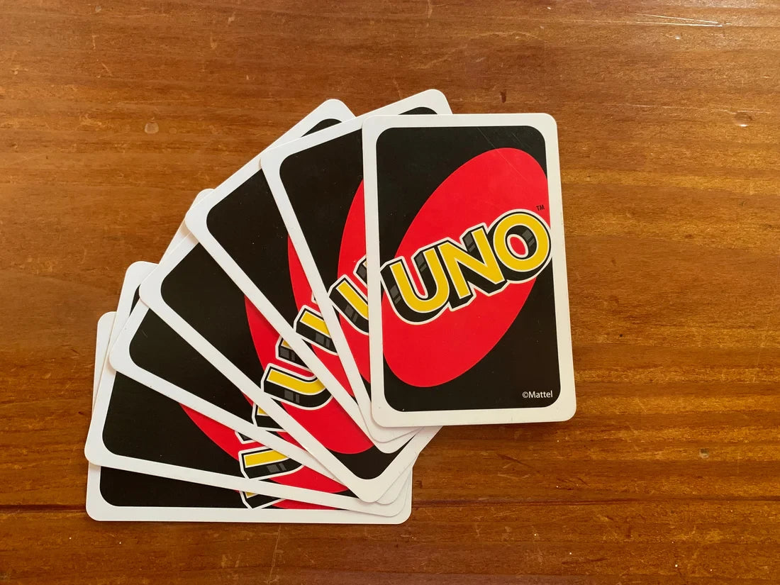 Desipan UNO card game with red and black cards fanned out on a wooden surface. Features the iconic UNO logo.