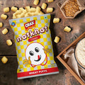 Desipan CRAX Natkhat Classic Wheat Puffs snack bag with a cartoon face, surrounded by puffs and wheat grains.